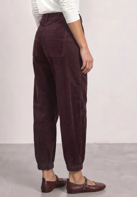 Rückenansicht einer Person mit bordeauxroter Cordhose, elastischen Bündchen und braunen Loafers.