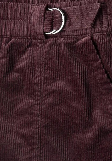 Nahaufnahme einer bordeauxroten Cordhose mit elastischem Bund, Tasche und D-Ring-Gürtel.