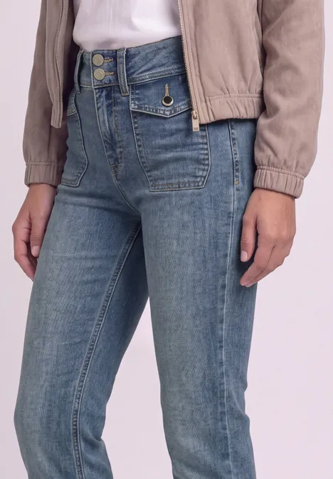 High Waist Bootcut Jeans im Slim Fit Mid Blue Washed Person in heller Jacke und hoch taillierter blauer Jeans mit Zierknöpfen, sichtbar bis zu den Oberschenkeln.