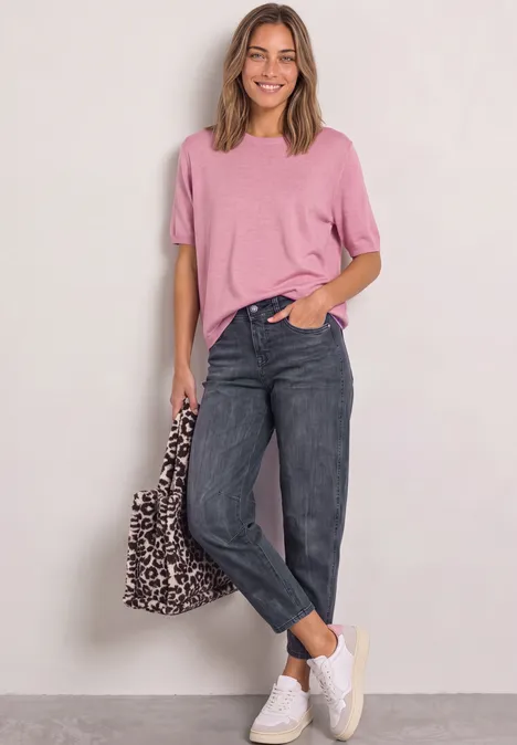 Frau in rosa Shirt, schwarzen Jeans und weißen Sneakern mit Leoparden-Tasche.