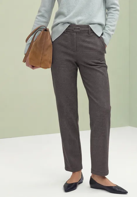 Person trägt grauen Pullover, dunkelbraune Hose, schwarze Ballerinas und hält eine cognacfarbene Tasche.
