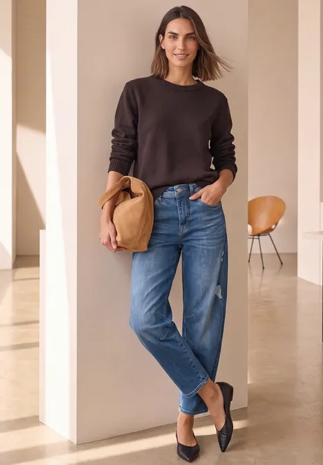 Relaxed Barrel Leg Jeans im Loose Fit Medium Blue Destory Washed Frau in braunem Pullover und Jeans mit Strohhut in heller, minimalistischer Umgebung.