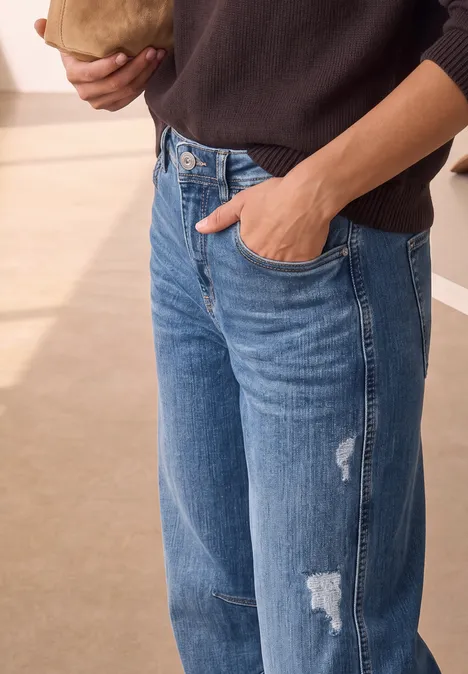 Relaxed Barrel Leg Jeans im Loose Fit Medium Blue Destory Washed Eine Person in blauen Jeans steckt die Hand in die Hose, Oberkörper teils sichtbar.