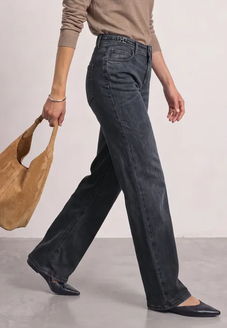 Frau geht, trägt schwarze weite Jeans, schwarze Ballerinas und eine beige Schultertasche.