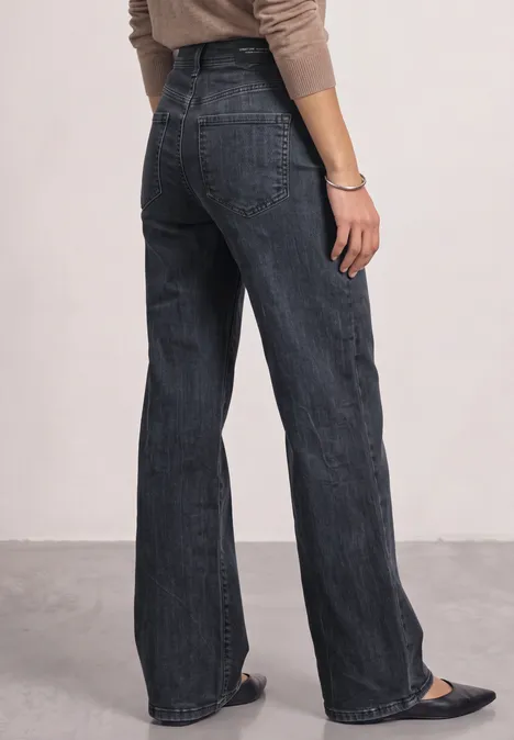 Eine Person von hinten trägt ein beiges Oberteil und dunkelblaue, weite High-Waist-Jeans.