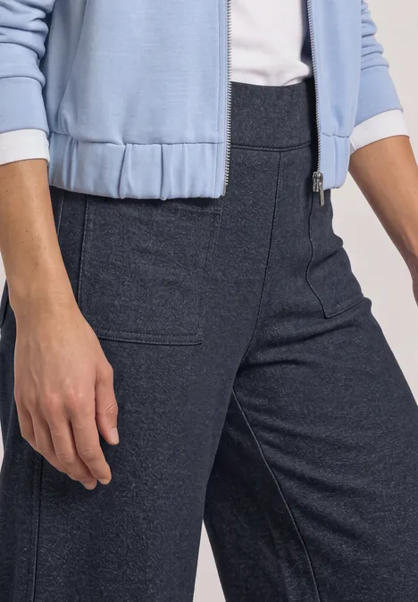 Eine Person trägt dunkelblaue, hochgeschnittene Hose mit seitlichen Taschen und hellblauem Oberteil.