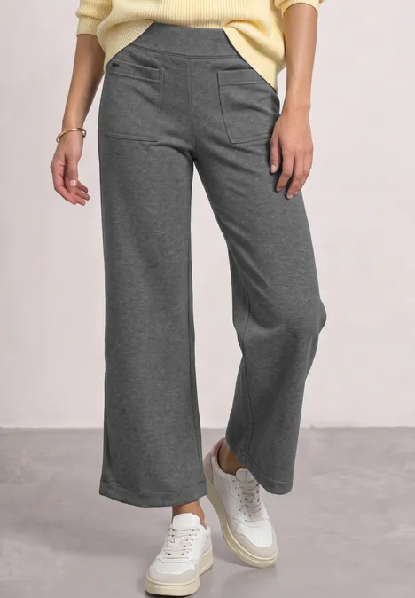 Grijze, wijde broek met hoge taille, gecombineerd met witte sneakers voor een casual uitstraling.