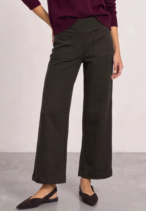 Person trägt weite, dunkelgraue, knöchellange Hose mit seitlichen Taschen und schwarze Slingback-Ballerinas.