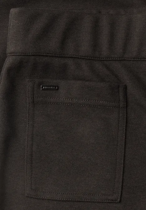 Nahaufnahme einer dunklen Hose mit eckiger aufgesetzter Tasche und kleinem Markenlogo.