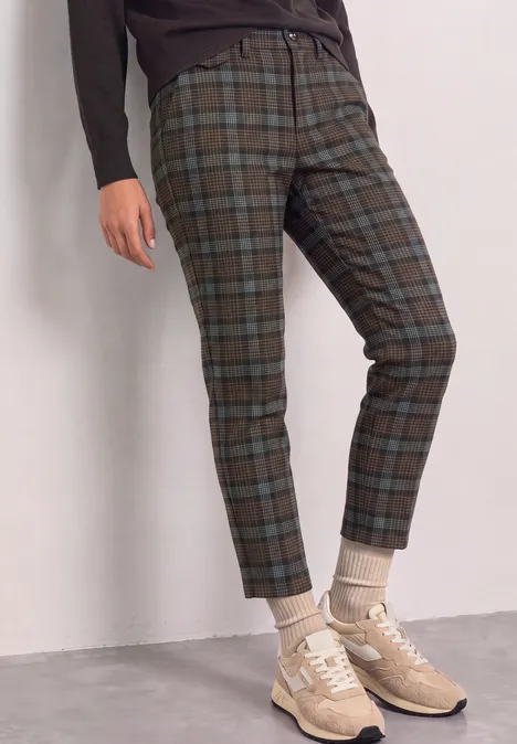 Person trägt karierte Hose (grün/blau) mit gekrempeltem Saum, beige Sneaker und Socken.