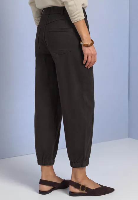 Pantalon noir taille haute à ourlets élastiques, associé à des mocassins marron plats, devant un mur clair.