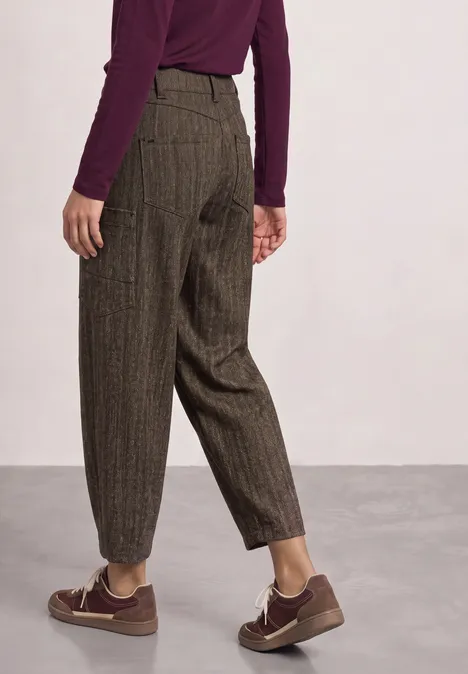 Persoon van achteren in een losse, bruine pantalon met fijne strepen, een bordeaux top en bruine sneakers.