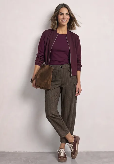Vrouw in stijlvolle herfstoutfit: paarse top en jas, geruite broek, bruine schoenen en bijpassende tas.