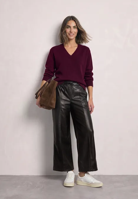 Straight Leg Hose in Leder-Optik black coffee Frau vor hellem Hintergrund, trägt schwarze XXL-Lederhose, burgunderfarbenen V-Pullover, weiße Sneaker und braune Tasche.