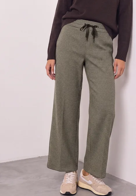 Wide Leg Hose mit Gallonstreifen und Dessin sanded amber Damenhose in Olivgrün mit weitem Bein und schwarzem Kordelzug, kombiniert mit einer dunklen Oberbekleidung.