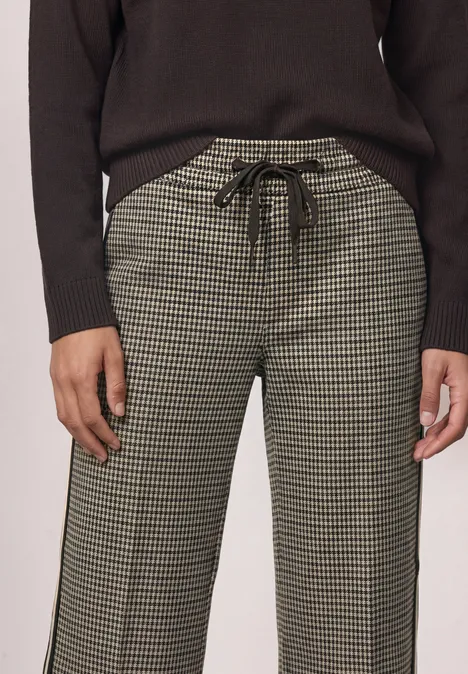 Wide Leg Hose mit Gallonstreifen und Dessin sanded amber Eine Person trägt eine Hose im Hahnentritt-Muster mit Tunnelzug und einen schwarzen Pullover.