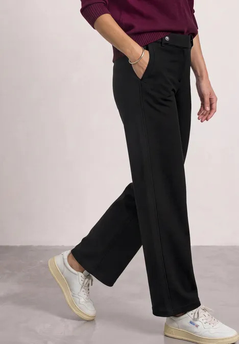 High Waist Wide Leg Hose im Casual Fit Black Seitliche Ansicht: Person trägt schwarze, weite Hosen und weiße Sneaker.