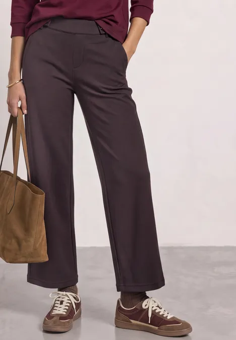 High Waist Wide Leg Hose im Casual Fit ruby vine Eine Person trägt weite braune Hosen, braune Sneaker und hält eine braune Veloursledertasche.