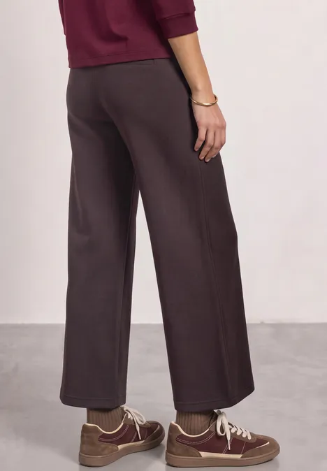 High Waist Wide Leg Hose im Casual Fit ruby vine Seitliche Rückansicht einer Person in brauner, locker geschnittener Hose, braunen Sneakern und bordeauxfarbenem Oberteil.