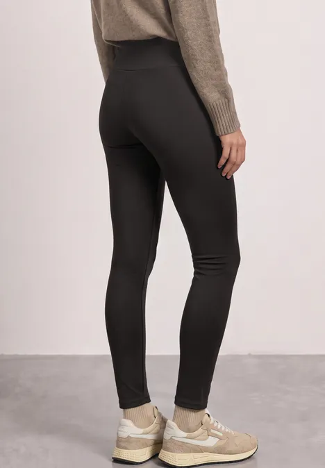 Thermo-Leggings im Skinny Fit black coffee Frau von hinten in figurbetonten schwarzen Leggings und beigen Sneakern.