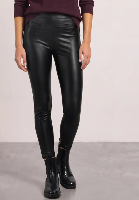 Figuur draagt zwarte leren legging en zwarte enkellaarsjes.
