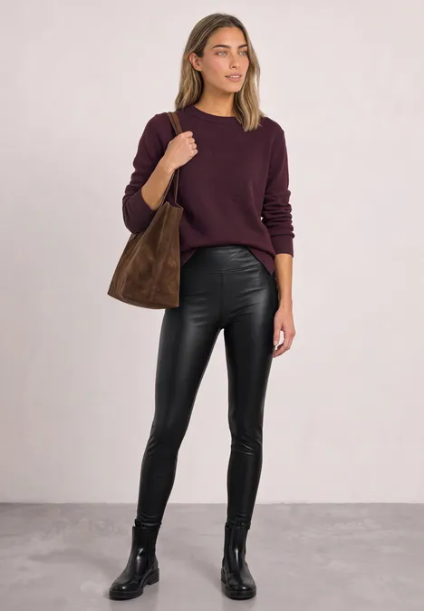 Een vrouw draagt een bordeaux trui, zwarte leren broek, zwarte laarzen en een bruine tas.