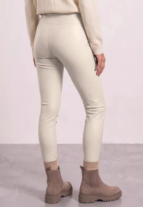 Vrouw van achteren in strakke beige legging en bruine laarzen voor een neutrale achtergrond.
