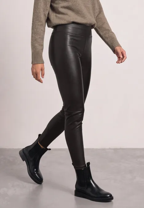 Schwarze Lederleggings und schwarze Chelsea-Boots im Studio-Setting, kombiniert mit beigem Pullover.