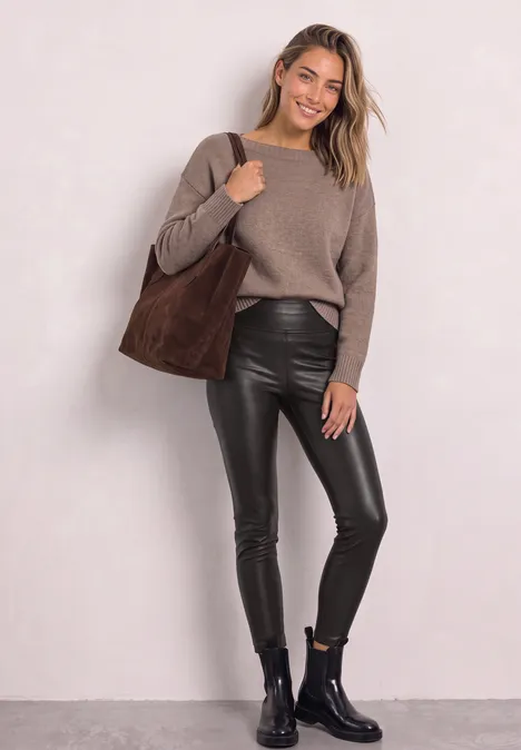 Junge Frau in lässigem Look: kuscheliger Pullover, schwarze Lederleggings, Stiefeletten und große Wildleder-Tasche.