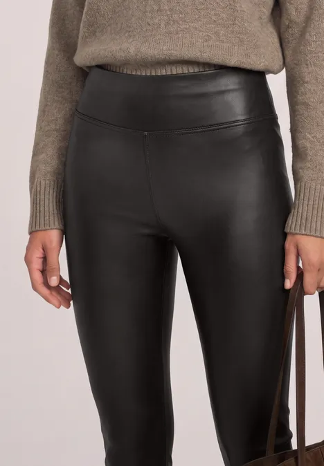 Schwarze, hochgeschnittene Lederleggings kombiniert mit grob gestricktem Pullover und Handtasche.