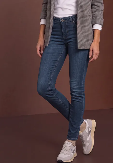Frau trägt dunkle enge Jeans, weiße Sneakers, weiße Bluse und graue Jacke