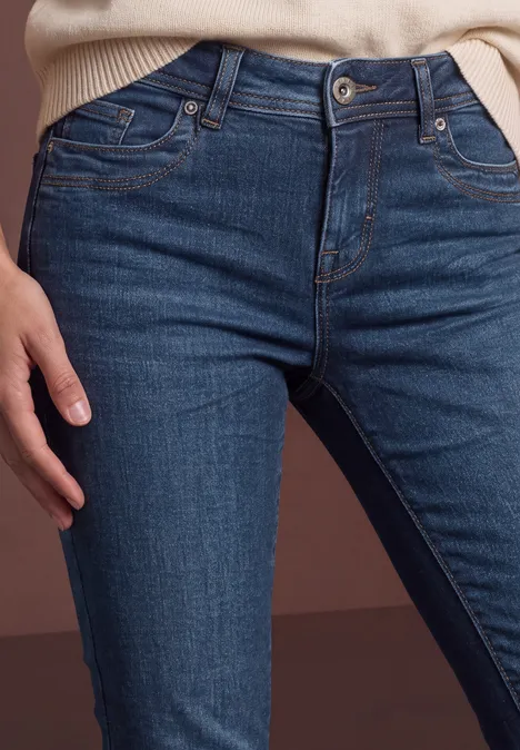 Mid Waist Straight Leg Jeans w kroju Slim Fit dark blue soft wash Zbliżenie osoby w ciemnych jeansach z ręką na biodrze na neutralnym tle.