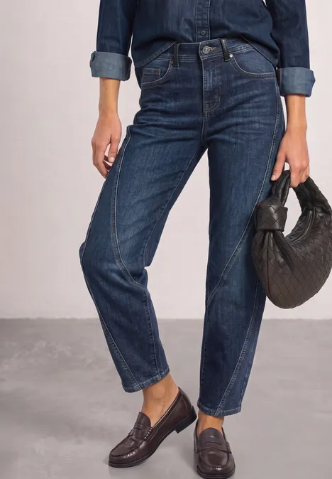 Dżinsy z luźnymi nogawkami typu „Loose Fit Barrel Leg” Dark blue authentic washed Kobieta w ciemnych, prostych dżinsach, granatowej koszuli i mokasynach, trzyma czarną torebkę.