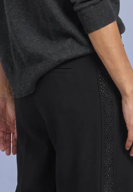 Zijaanzicht van een persoon met een zwarte broek met studdetail en een donkergrijze trui.