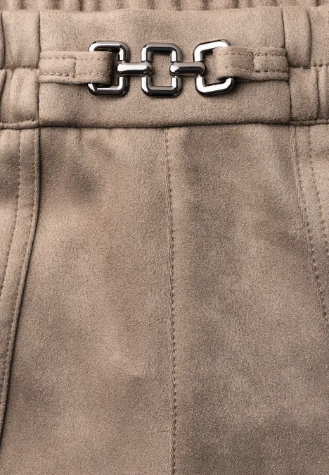 Nahaufnahme einer hellbeigen Wildlederhose mit silberner Kettendekoration am Bund