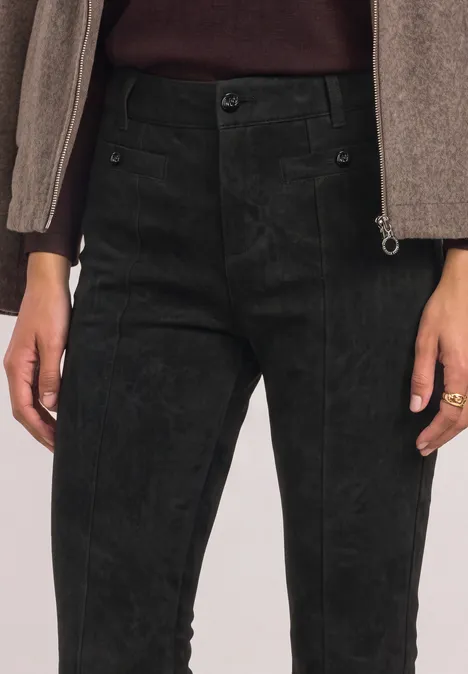 Schwarze Cordhose auf Taillenhöhe, kombiniert mit beigem Oberteil und Ring am Finger.