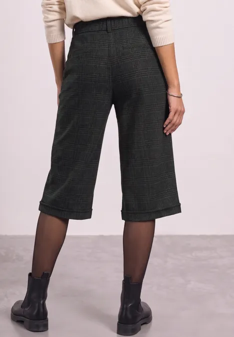 Rückansicht einer Person in weiten, midilangen grünen Culottes, schwarzen Strumpfhosen und schwarzen Boots.