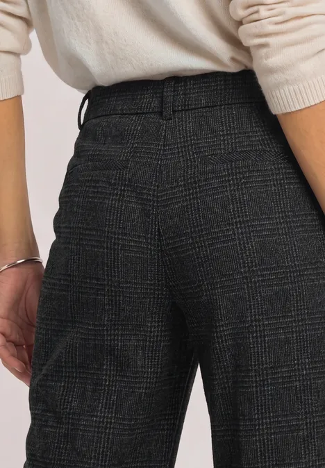 Rückenansicht einer Person in cremefarbenem Pullover und karierten, dunkelgrauen Stoffhosen.