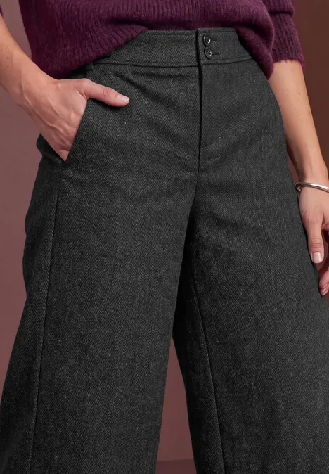 Gros plan d'une personne en pantalon gris anthracite à jambes larges, main dans la poche