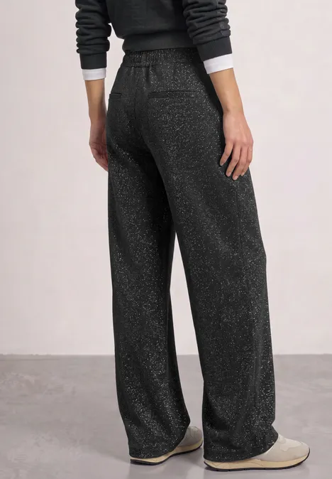Foto einer von hinten gezeigten Person in dunkelgrauen, weiten Lounge-Hose mit Glitzereffekt und Hausschuhen.