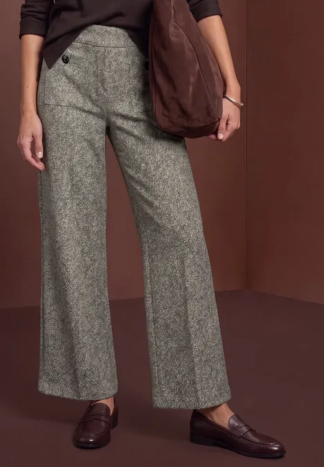 Eine Person trägt graue, weit geschnittene Hose, braune Loafers und eine lässige Schultertasche.