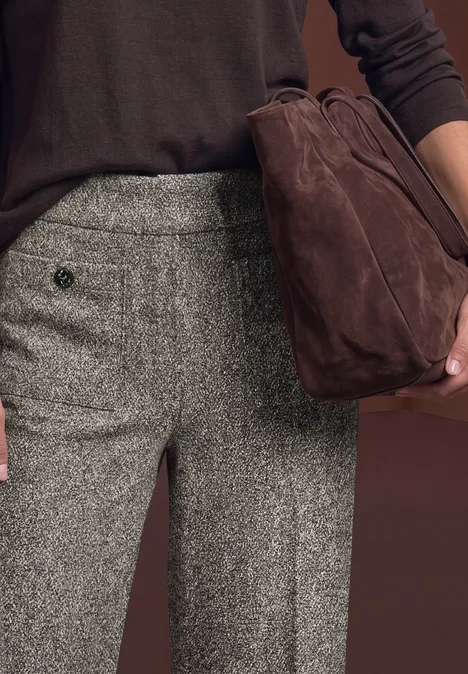Hose aus grauem Tweed und dunkelbrauner Pullover, dazu eine braune Wildledertasche in der Hand.