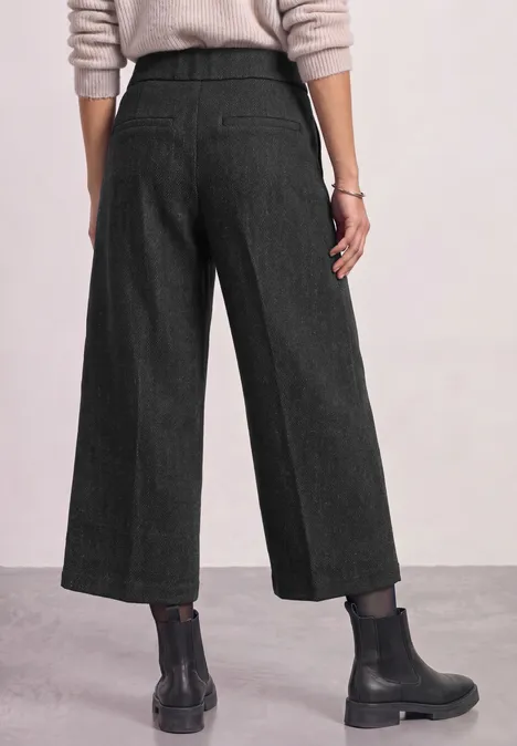 Vue de dos : pantalon large noir aux chevilles, pull clair et bottines noires.