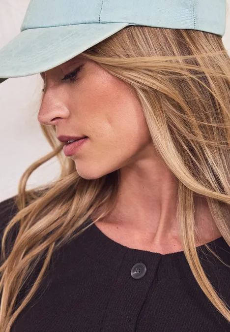 Personne aux longs cheveux blonds, casquette bleu clair et vêtement sombre, visage flou.