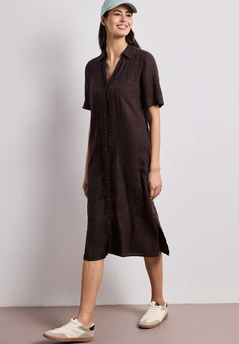 Femme en robe-chemise midi marron foncé, manches courtes, fentes latérales, baskets beiges et casquette.