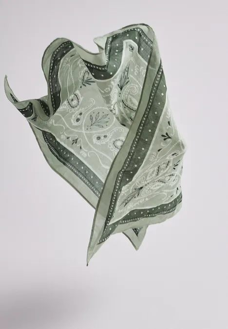 Ein grünes Halstuch mit Paisley-Muster schwebt vor hellem Hintergrund.