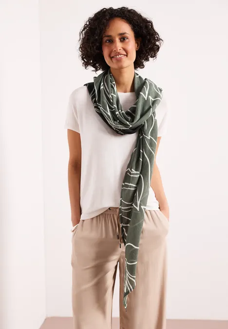 Eine Person trägt ein weißes T-Shirt, eine beige Hose und einen grünen Schal um den Hals.