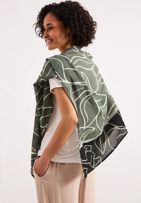 Seitlich abgebildete Person mit lockigem Haar trägt ein grünes Tuch mit weißem Muster über die Schultern.