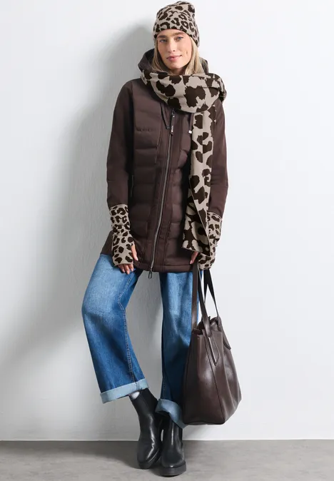 Frau in brauner Steppjacke mit Animal-Print-Schal, weiten Jeans, schwarzen Boots und brauner Tasche.