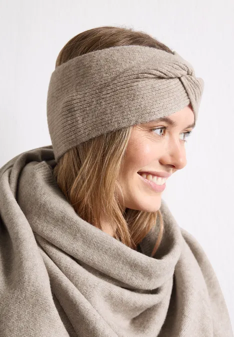 Feinstrick Stirnband in Unifarbe Soft Sand Mel. Eine lächelnde Frau mit einem beigefarbenen Strickstirnband und passendem Wollschal.